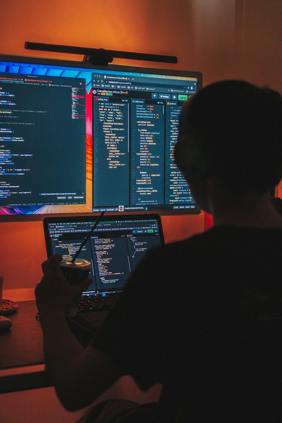Programador a contraluz en una pared de oficina, trabajando en pantallas de ordenador.