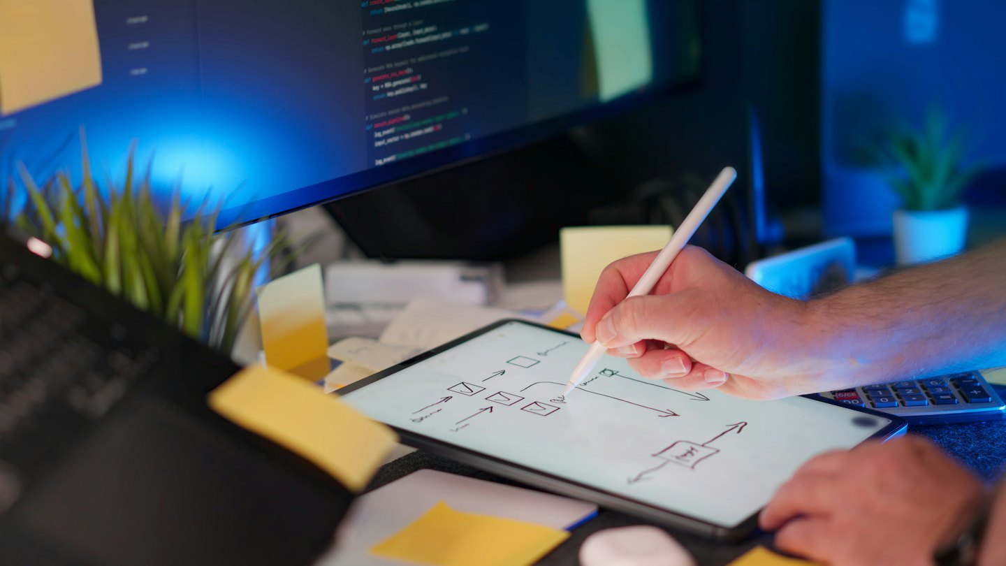 Mano usando un lápiz óptico para dibujar un diagrama de flujo en una tableta con un monitor de computadora.